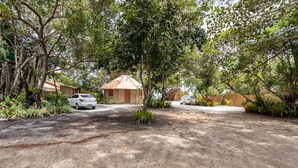 A residential area with a dirt driveway, a corrugated metal-roofed house, and a white car parked in the background. - Beachfront Cabins in Bahia – OTX (Porto Seguro)