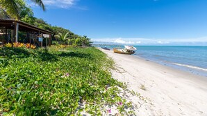 A beach with a wooden structure, a boat, and lush greenery. - Beachfront Cabins in Bahia – OTX (Porto Seguro)