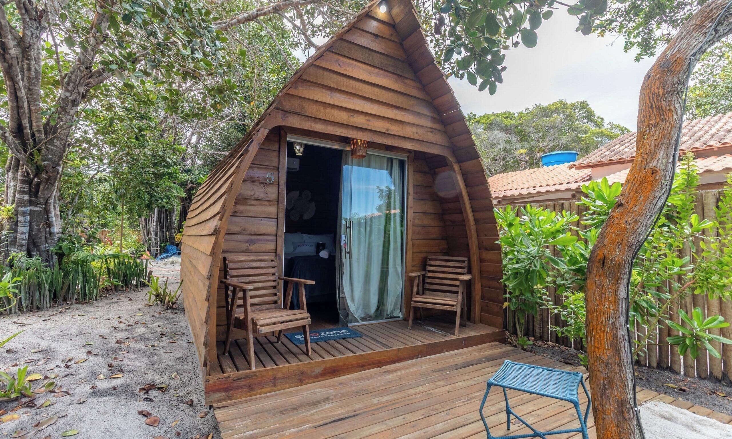 A wooden cabin with a sloped roof, a porch with two chairs, and a wooden deck.