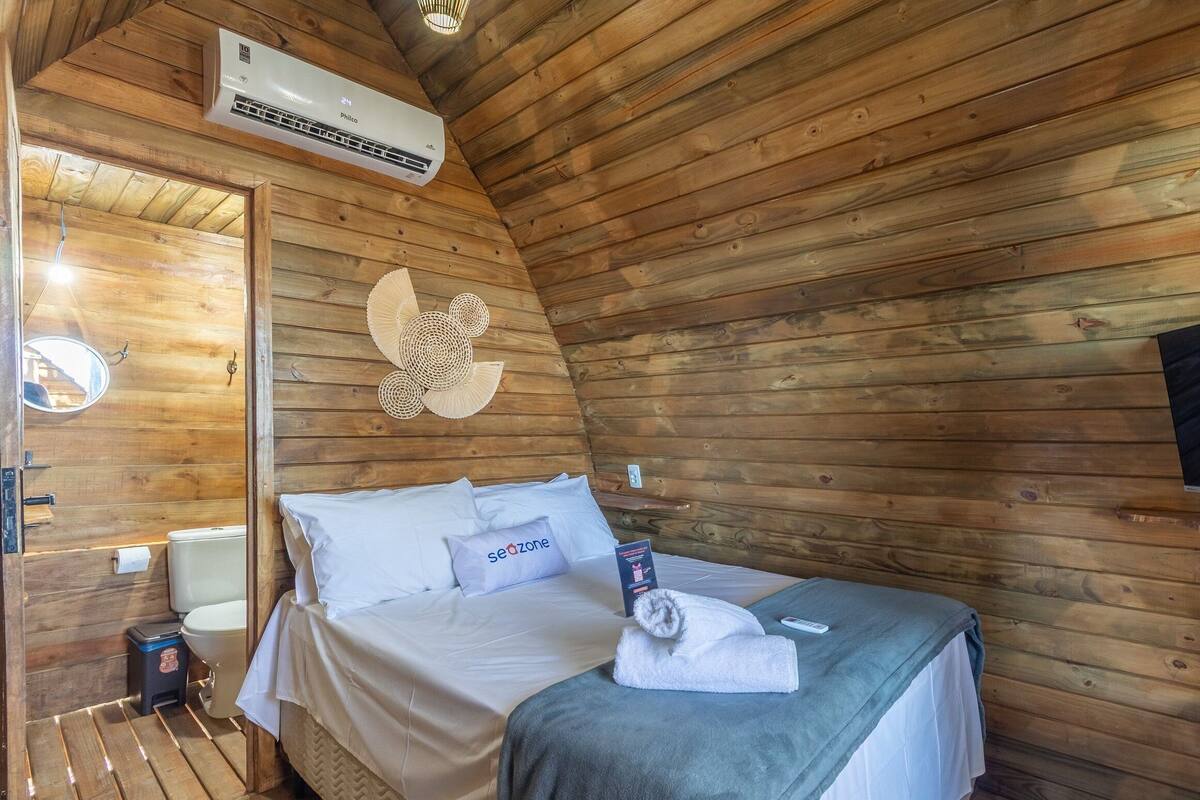 A wooden cabin room with a bed, a wall-mounted air conditioner, a mirror, and a wall decoration.