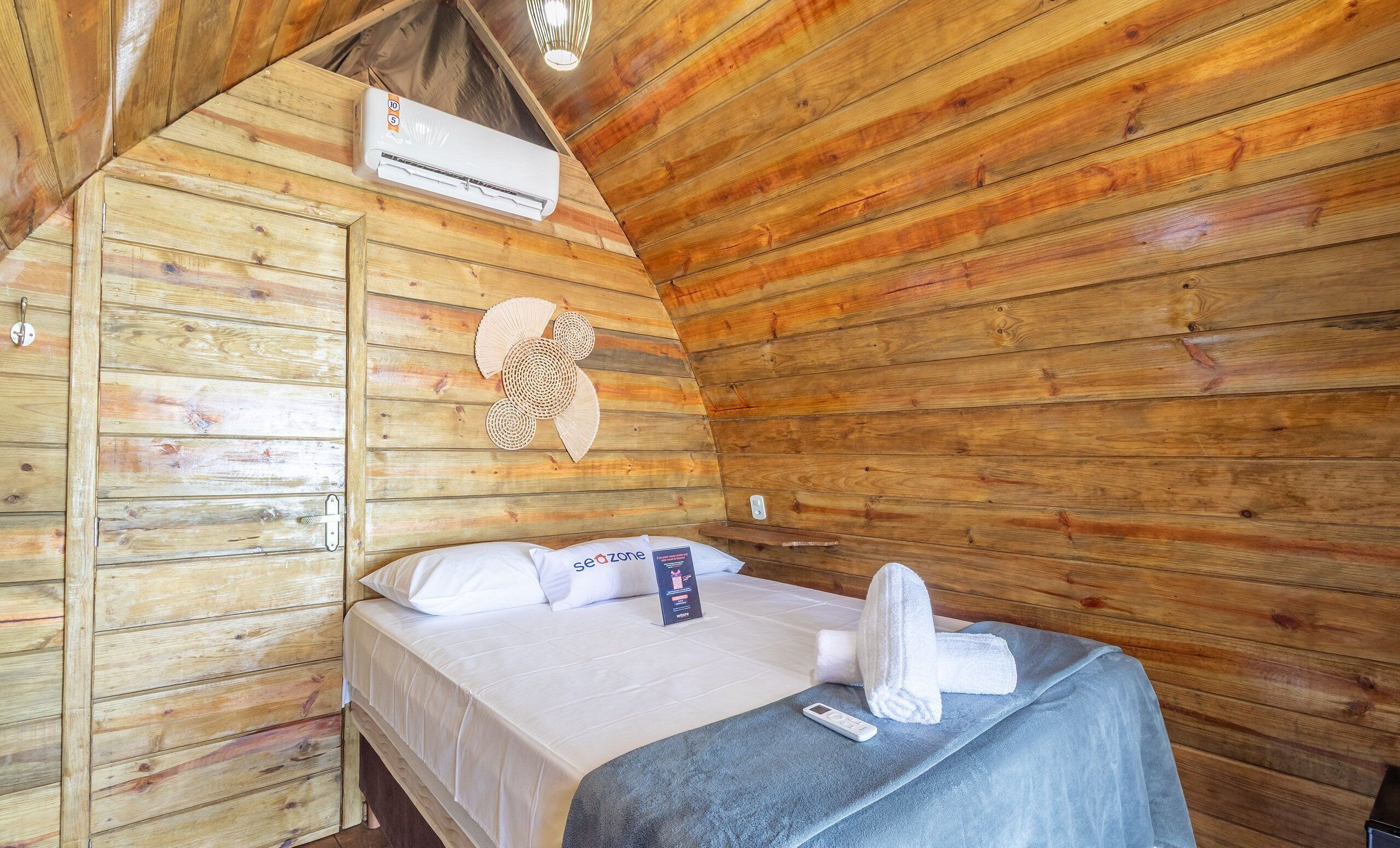 A wooden cabin room with a bed, a wall-mounted air conditioner, and a woven wall decoration.