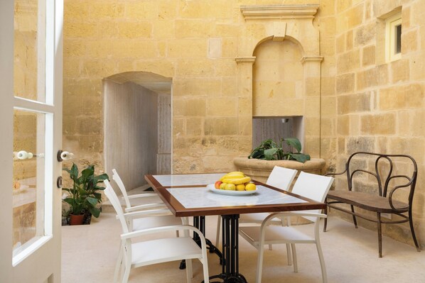 A dining area with a marble table, white chairs, and a fruit plate.