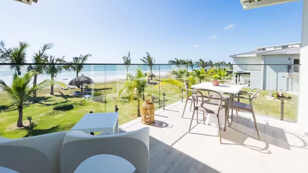 Een balkon met uitzicht op het strand, zitplaatsen buiten en een glazen hekwerk.