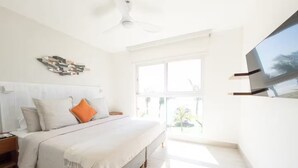 Een slaapkamer met een bed, nachtkastjes, een plafondventilator, een groot raam en een aan de muur bevestigde televisie.