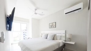 A modern bedroom with a large bed, a ceiling fan, an air conditioning unit, and a TV mounted on the wall.