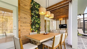 A modern dining area with a wooden table and white cushioned chairs, a vertical garden wall, and wicker pendant lights. - Mario | Minions | Theater | Private Pool | Disney 15883 (Clermont)