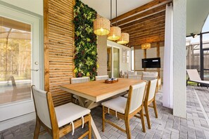 Ein moderner Essbereich mit einem Holztisch, weiß gepolsterten Stühlen, einer vertikalen Gartenwand und Korbtropfleuchten.