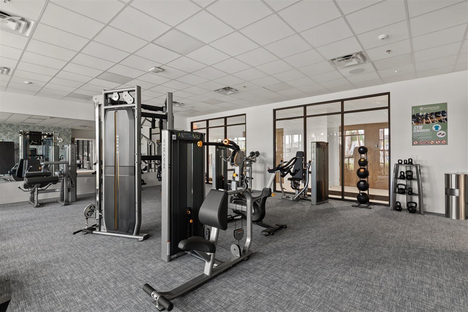A gym with various exercise equipment, a mirrored wall, and a large window.