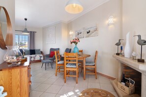 A living room with a dining area, a fireplace, and a large window. - Ria's Birds in Cabanas de Tavira – Comfort and Nature by the Ria Formosa (Cabanas de Tavira)