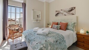 A bedroom with a bed, a bedside table, a nightstand, a chair, a window, and a wall-mounted mirror. - Ria's Birds in Cabanas de Tavira – Comfort and Nature by the Ria Formosa (Cabanas de Tavira)