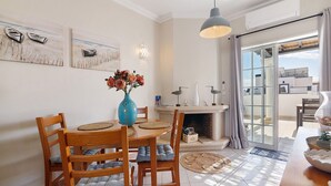 A dining area with a wooden table, chairs, a vase with flowers, and artwork on the wall. - Ria's Birds in Cabanas de Tavira – Comfort and Nature by the Ria Formosa (Cabanas de Tavira)