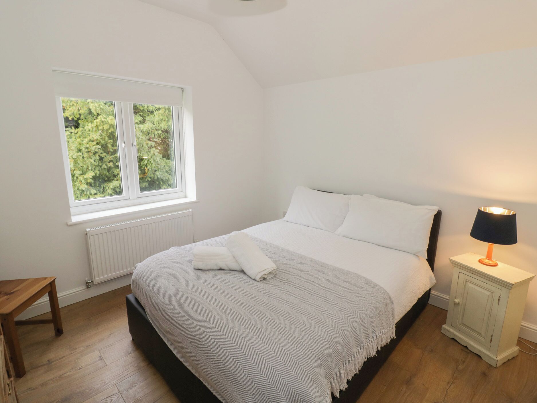 A bedroom with a bed, a nightstand, a window, and a radiator.