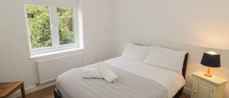 A bedroom with a bed, a nightstand, a window, and a radiator.