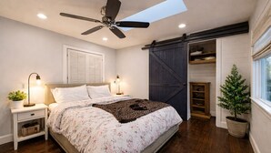 A bedroom with a bed, bedside tables, a ceiling fan, a skylight, a sliding barn door, a potted plant, and a window. - Charming 2-bedroom bed & breakfast in superb Seattle neighborhood (Seattle)