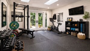 A gym with a bench, dumbbells, a squat rack, an exercise bike, and a TV on the wall. - Charming 2-bedroom bed & breakfast in superb Seattle neighborhood (Seattle)