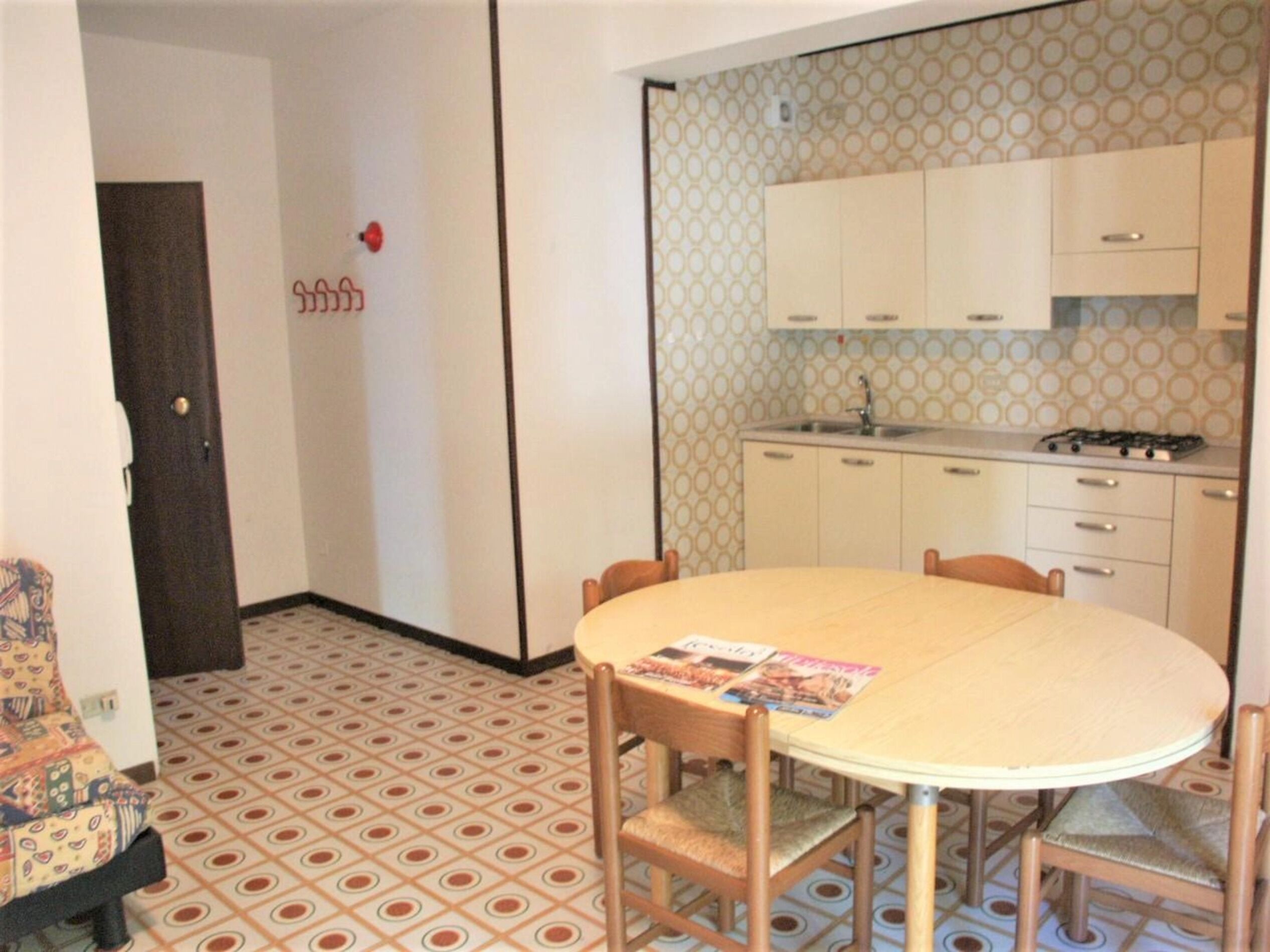 A compact kitchen with a round dining table, wooden chairs, and patterned floor tiles.