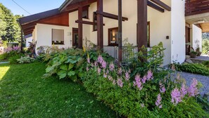 Uma casa moderna com varanda coberta, janelas amplas e um jardim bem cuidado, com diversas plantas e flores.