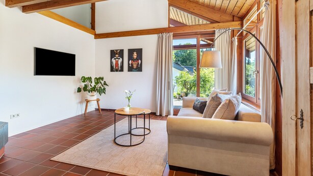 Uma sala de estar com sofá, televisão, planta e janela com cortinas.