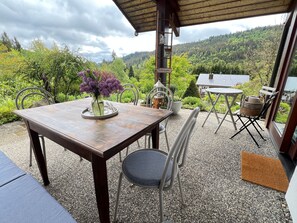 Et træbord med en vase blomster, en stol og udsigt til en skovklædt bakke.