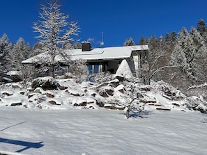 A snow-covered landscape with a house surrounded by trees and rocks.