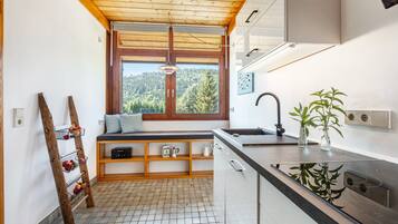 A compact kitchen with a window view, wooden shelves, and a built-in bench.