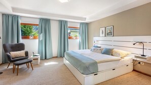Um quarto com cama, uma cadeira, mesa de cabeceira e janela com cortinas.
