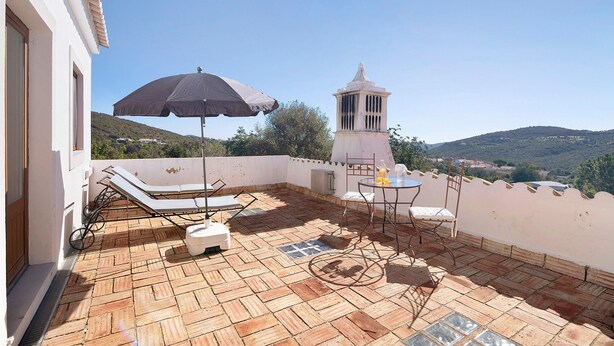 Une terrasse sur le toit, dotée d’un sol carrelé, de chaises longues, d’une table avec des chaises, d’un parasol et d’une petite structure en forme de tour.