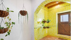Une pièce aux murs recouverts de carreaux jaunes, avec une porte en bois et des plantes suspendues.