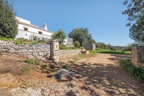 Une route de campagne mène à un bâtiment blanc doté d’un mur en pierre et d’une petite tour.