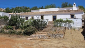 A white building with a tiled roof, stone steps, and a small garden area. - Apartment 'Paz E Natureza 3' with Wi-Fi (São Brás de Alportel)