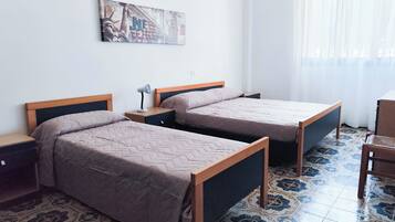 Quarto com duas camas de solteiro, mesa de cabeceira com abajur, uma mesinha e uma cadeira.