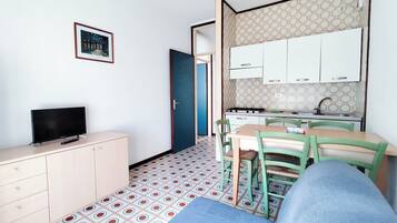 Un espacio habitable compacto con kitchenette, comedor y televisor.