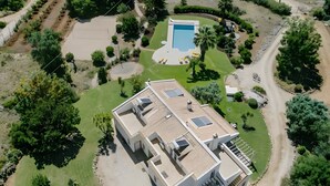 Una casa grande y moderna con piscina, rodeada de césped y árboles cuidados.