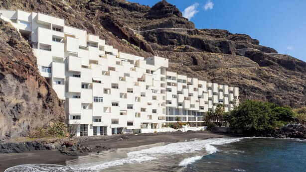 Un hotel costero de fachada blanca y moderna, ubicado en un acantilado rocoso con vistas al mar.