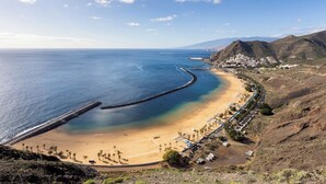 Vista costera con playa, un muelle y un pueblo al fondo.