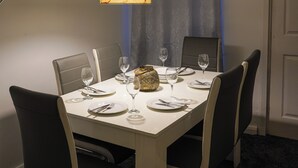 A dining table set for four with chairs, a decorative lamp, and a small gold item on the table. - Modern Family Home in Rotherham, Long-Stay Friendly. (Parkgate)