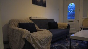 A cozy living room with a dark-colored sofa, a white table, and a patterned rug. - Modern Family Home in Rotherham, Long-Stay Friendly. (Parkgate)