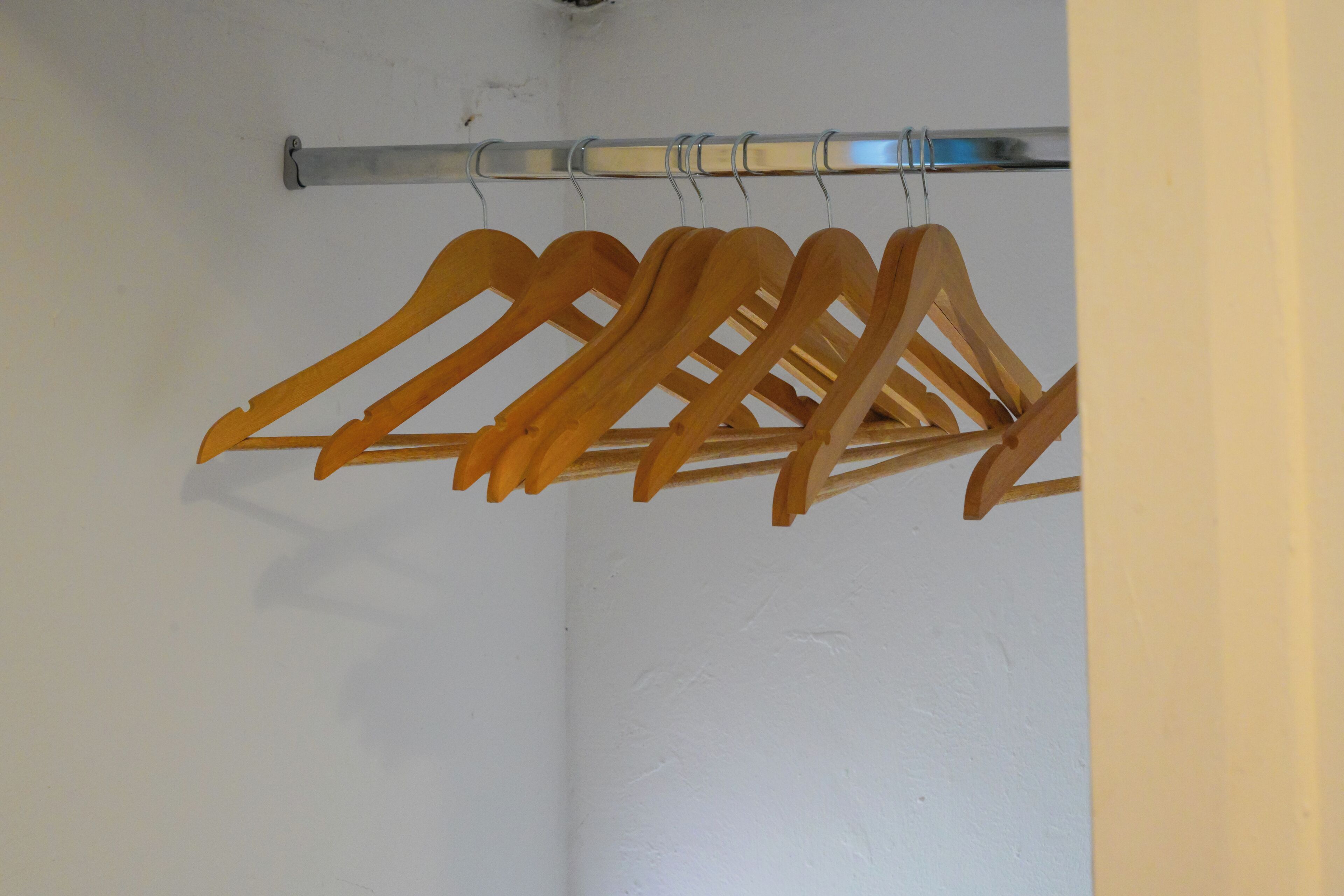 A closet with wooden hangers hanging on a metal rod.