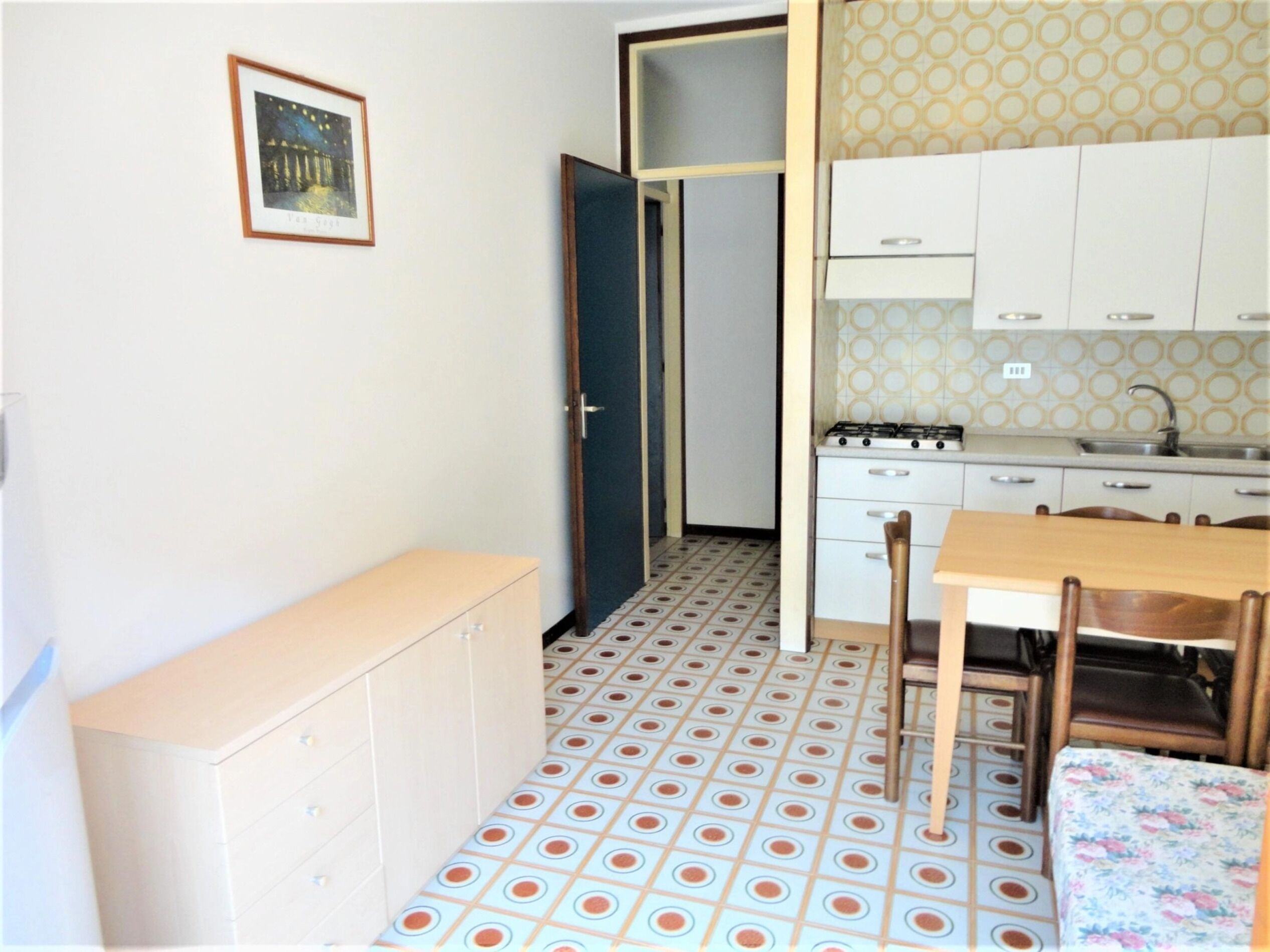 Une cuisine compacte avec un sol carrelé, une table à manger et un petit meuble de rangement.