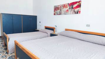 Quarto com duas camas de solteiro, um guarda-roupa azul, uma obra de arte na parede e piso estampado.