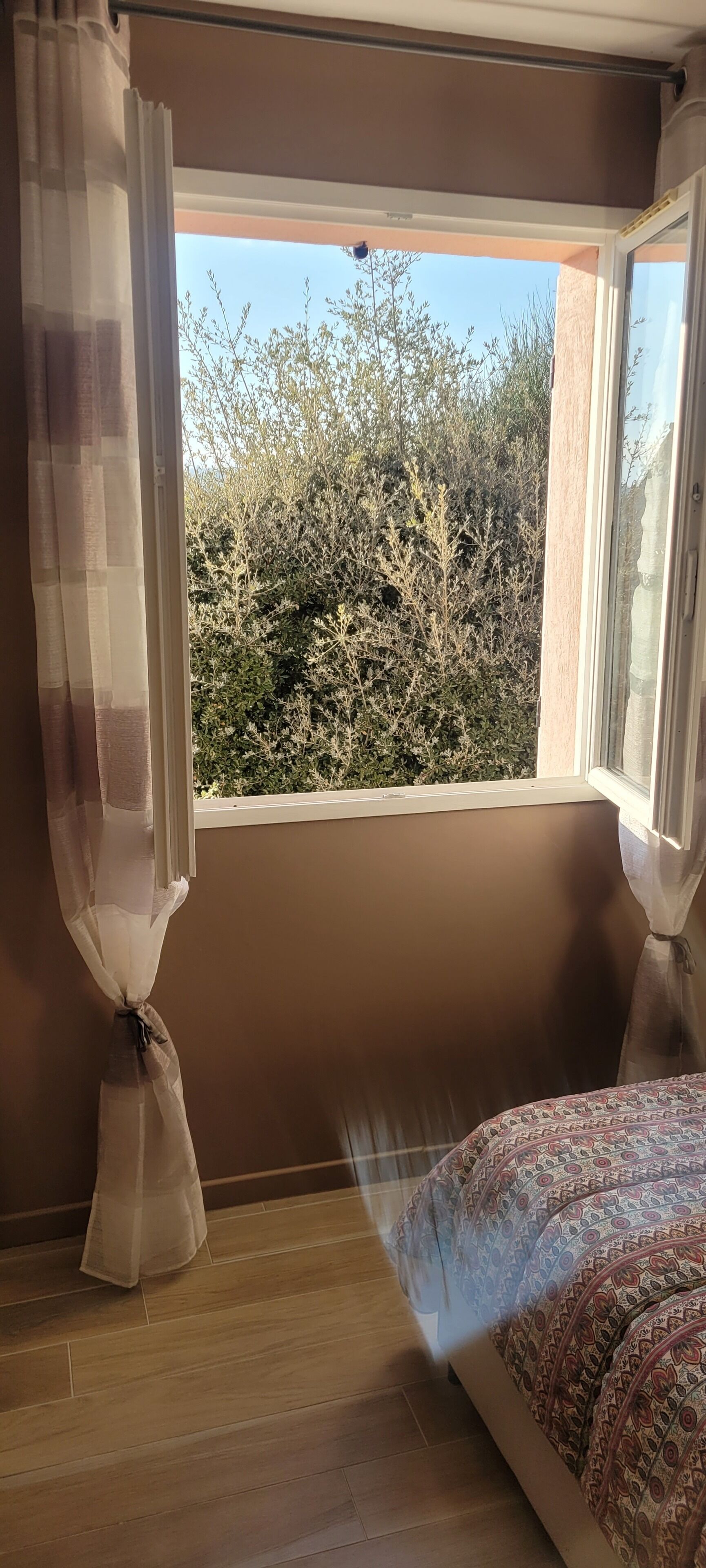 Una camera da letto con una finestra, un letto con copriletto decorato e una tenda legata in basso.