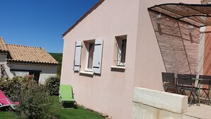 Ett rosa hus med ett tak täckt av tegelpannor, ett litet fönster med fönsterluckor och en uteplats med ett bord och stolar.