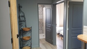 En hall med ett metallställ som håller korgar, en trädörr och ett badrum som syns genom en öppen dörr.