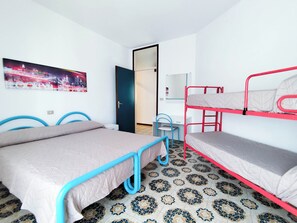A room with two beds, a desk, a chair, and a door leading to another room. - Comfortable Flat Near the Beach (Jesolo)