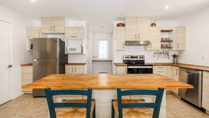 A modern kitchen with wooden cabinets, stainless steel appliances, and a central island with chairs. - Hôtel à la maison - Chez Charcole (Saint-Ferréol-les-Neiges)