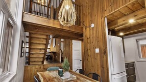 A rustic kitchen with wooden walls, a wooden dining table, and a hanging light fixture. - Hôtel à la maison - Entre Monts et Collines (Orford)