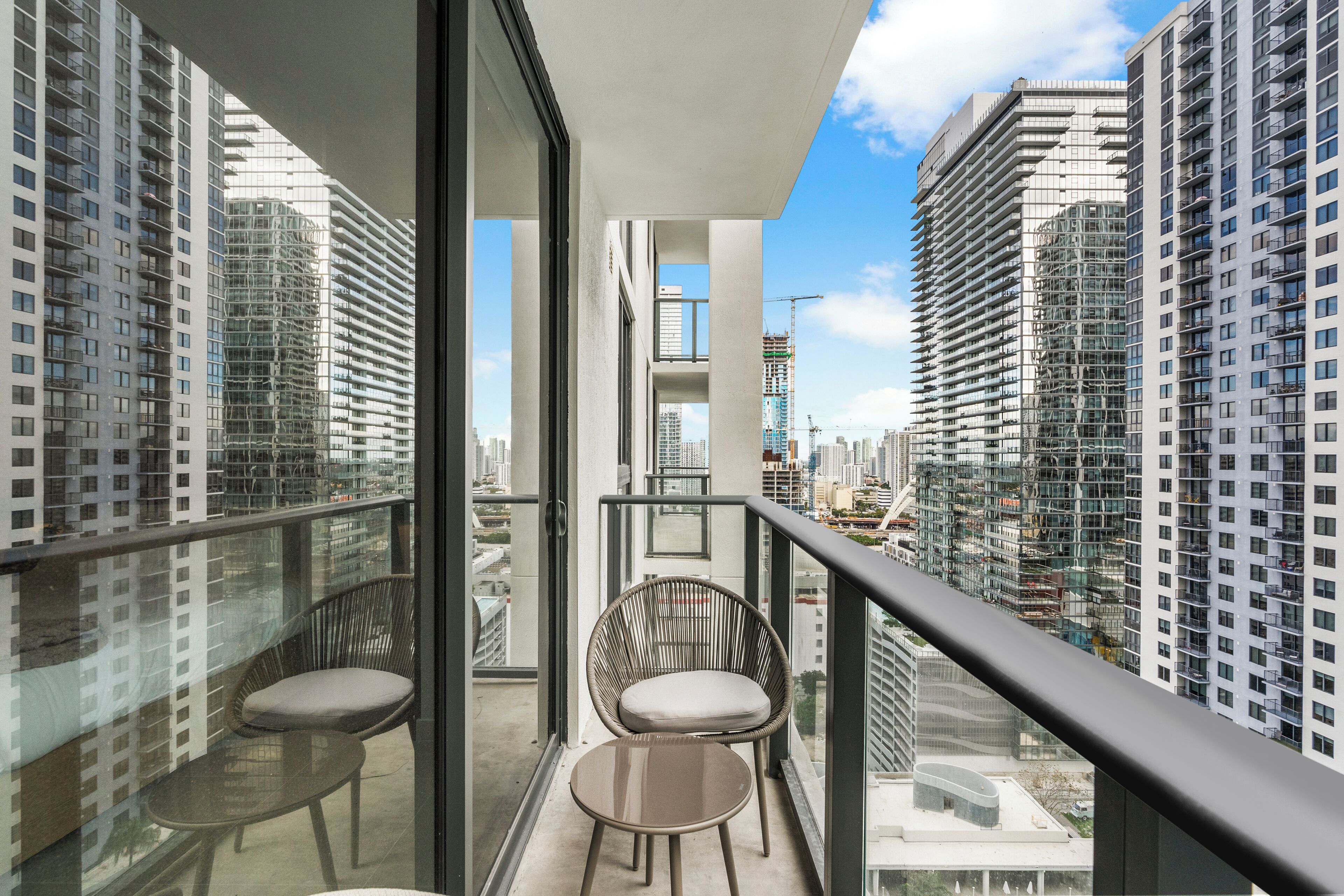 Een balkon met twee stoelen en een tafeltje, met uitzicht op een stadsbeeld met moderne wolkenkrabbers.