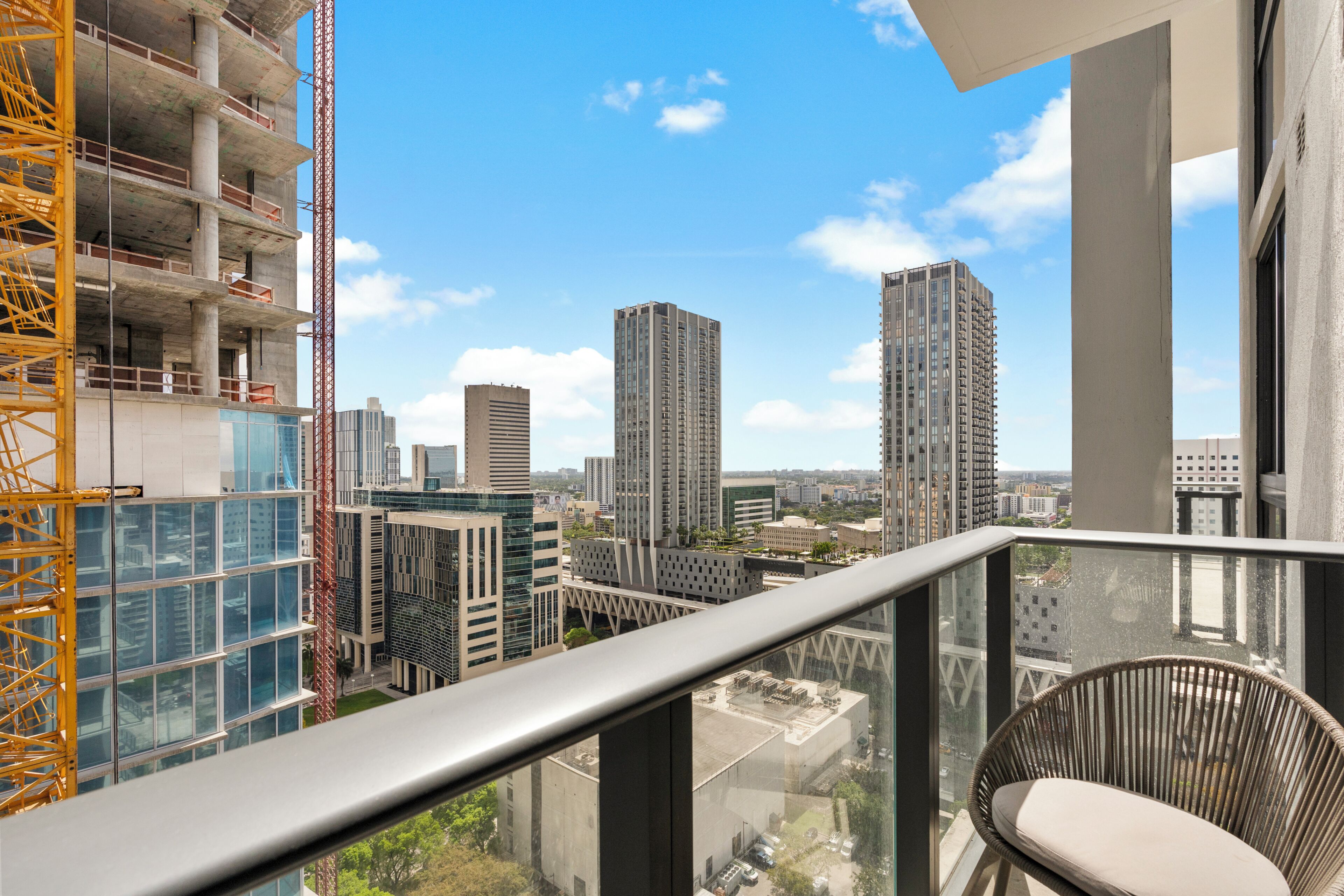 Un edificio alto con balcón, una grúa de construcción y arquitectura moderna circundante.