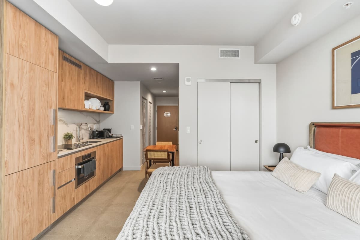 Une chambre compacte comprenant un lit, une table de chevet et un coin cuisine.