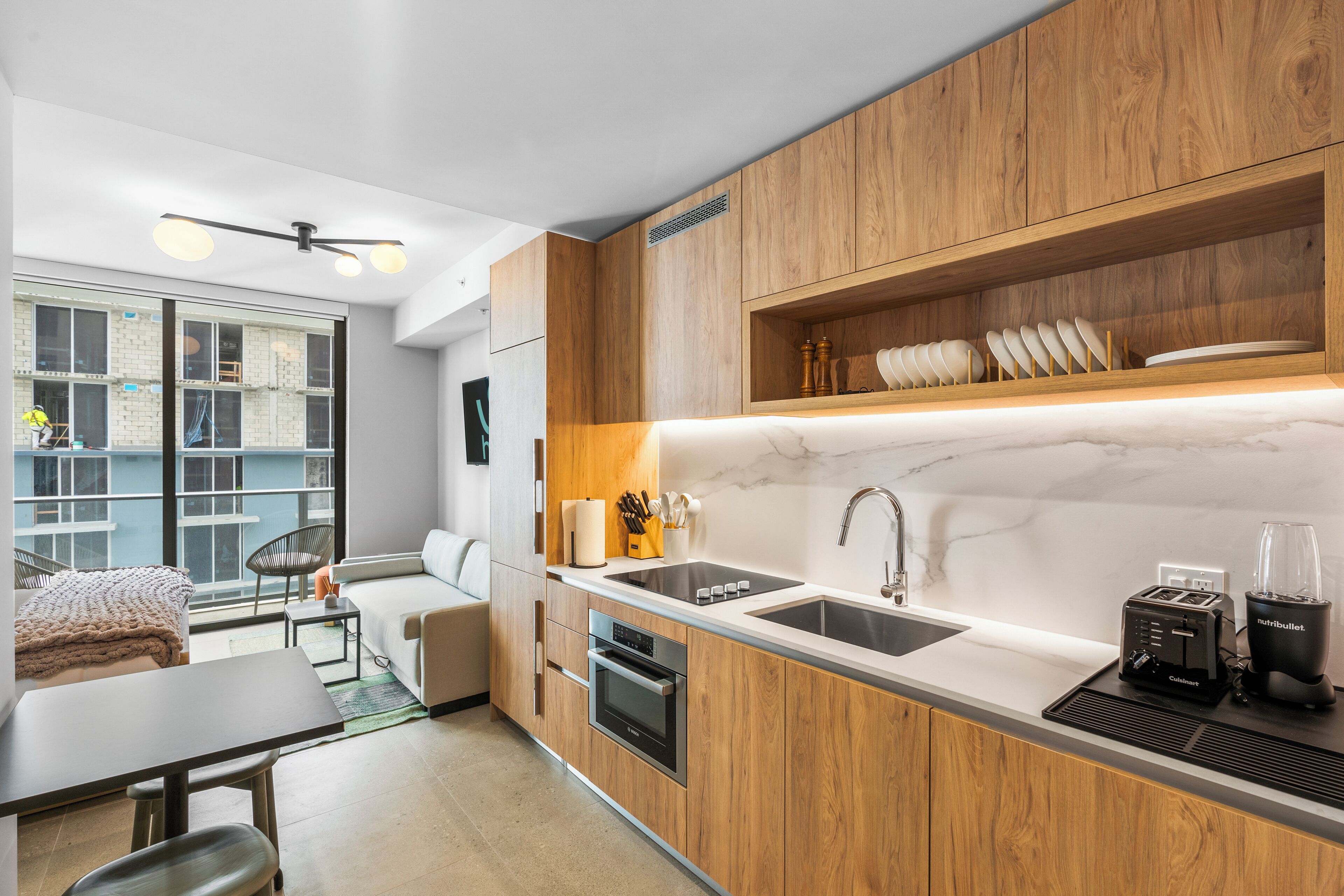 A modern kitchen with wooden cabinets, a marble countertop, a sink, and a built-in oven.